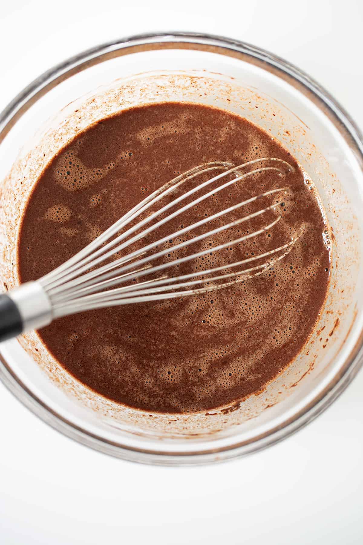 A glass bowl with a whisk and chocolate stout cake batter in it.