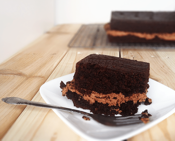 chocolate cake on a white square plate on a wooden surface.