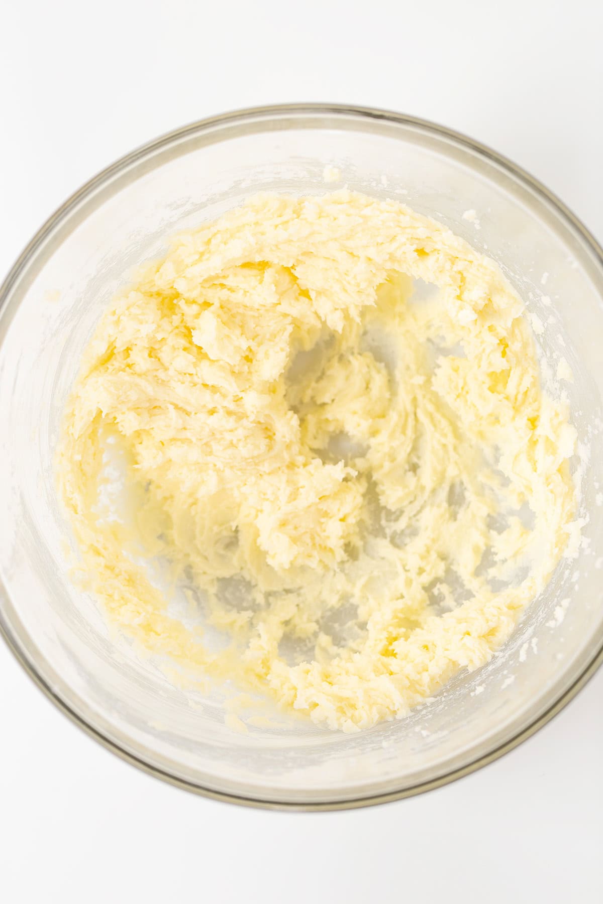 A glass bowl containing creamed butter and sugar mixture on a white surface, ready to become the delicious base for Oreo Cookies and Cream Cupcakes.