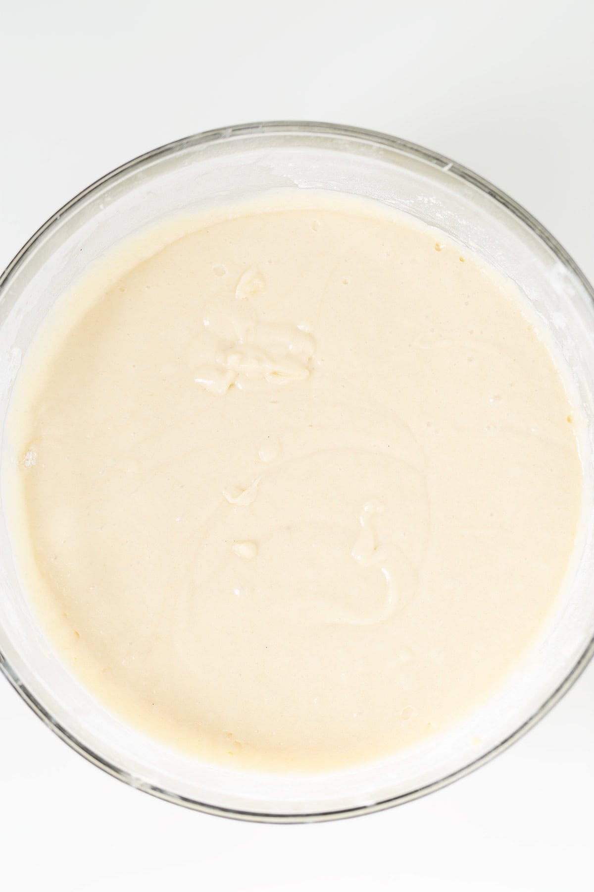 A glass bowl filled with smooth, creamy batter for Oreo Cookies and Cream Cupcakes sits on a white surface.