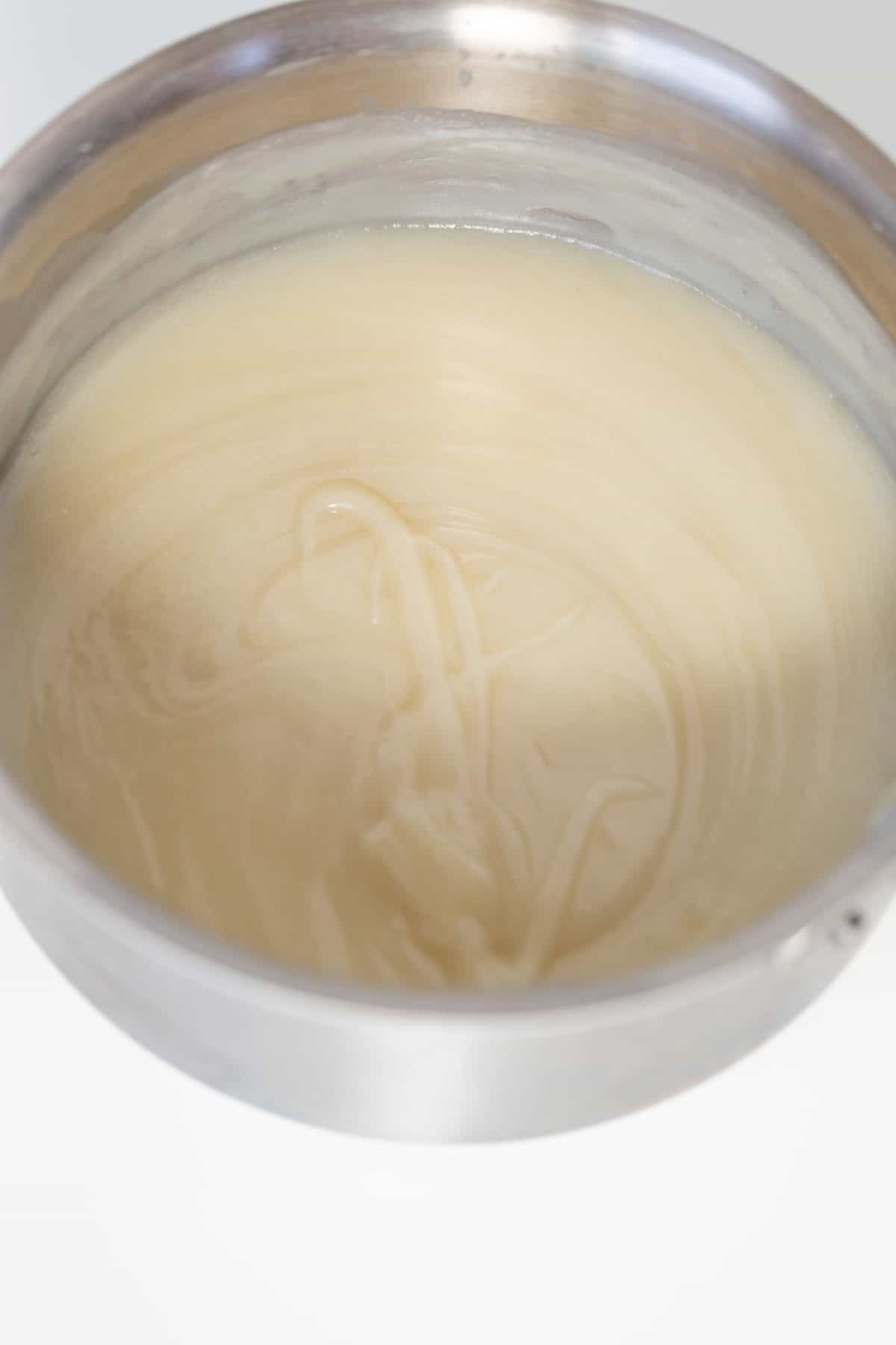 A stainless steel bowl filled with smooth, pale Oreo Cookies and Cream Cupcakes batter rests on a white surface.