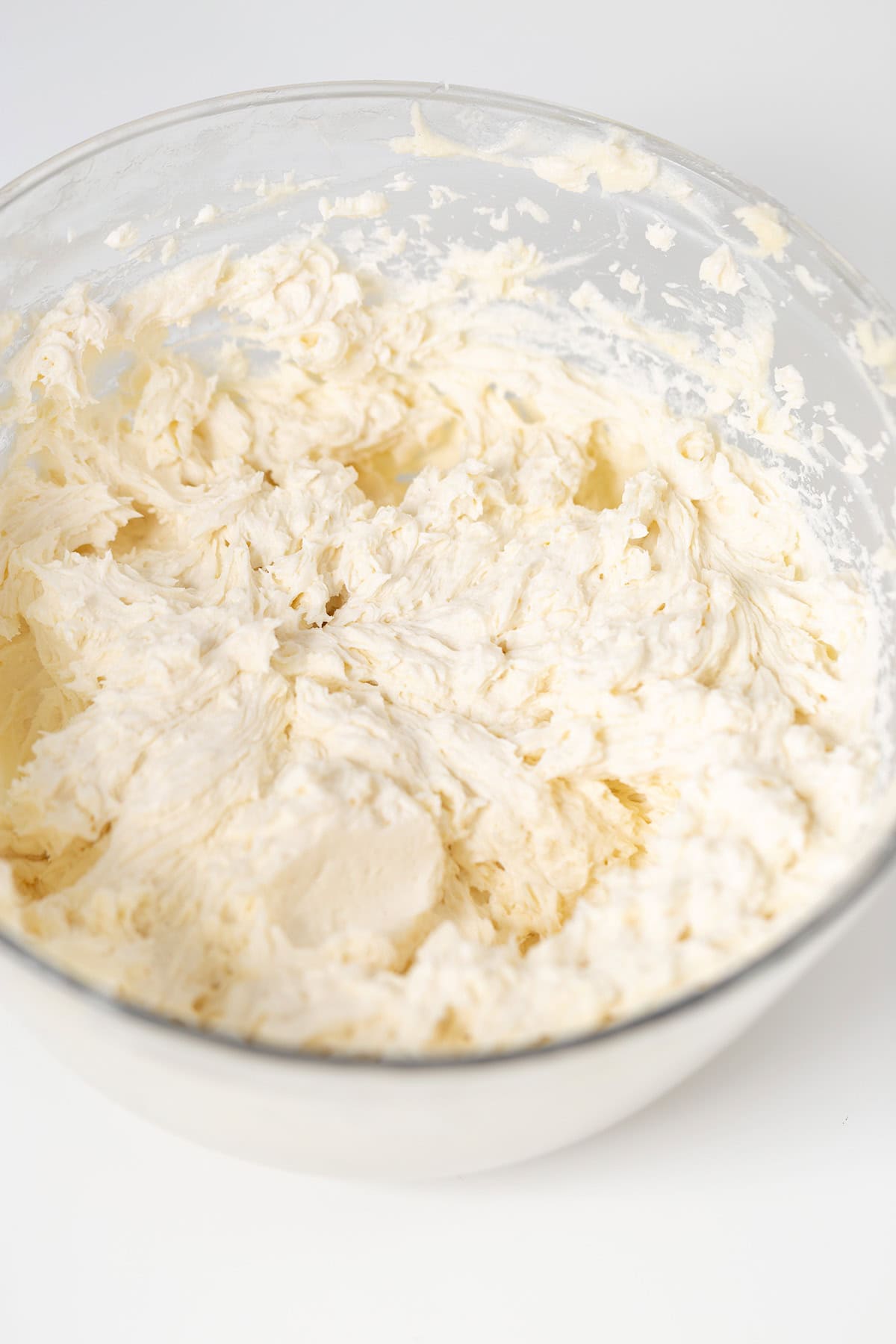 A glass bowl filled with whipped, creamy white frosting, with visible peaks and swirls on its surface—perfect for topping Oreo Cookies and Cream Cupcakes.