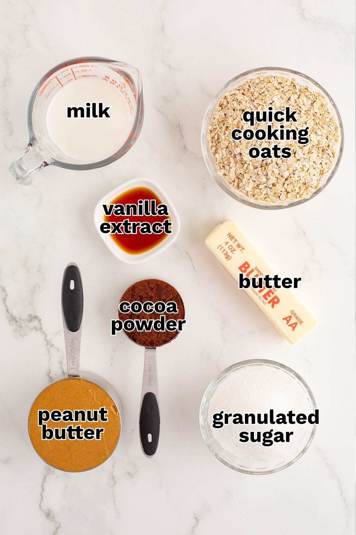 Ingredients for Chocolate No-Bake Cookies displayed on a white surface: milk, quick cooking oats, butter, vanilla extract, cocoa powder, peanut butter, and granulated sugar.
