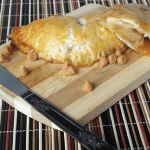 A knife cutting through apple hand pies on a wooden cutting board.