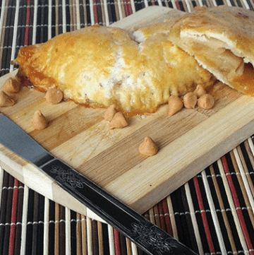 A knife cutting through apple hand pies on a wooden cutting board.