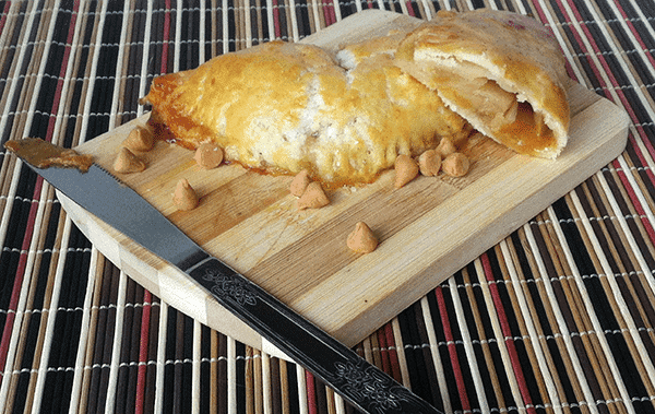 A knife cutting through apple hand pies on a wooden cutting board.