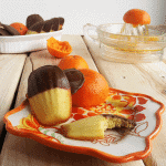 A plate of chocolate covered oranges with orange madeleines on a wooden table.