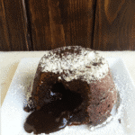 A decadent chocolate lava cake on a plate with powdered sugar.