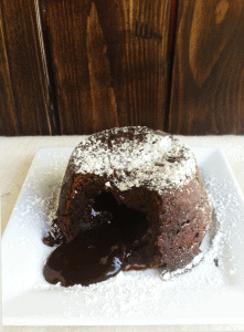 A decadent chocolate lava cake on a plate with powdered sugar.