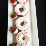Baked Strawberry Donuts with sprinkles and white chocolate ganache on a plate.