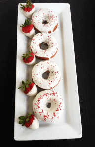 Baked Strawberry Donuts with sprinkles and white chocolate ganache on a plate.