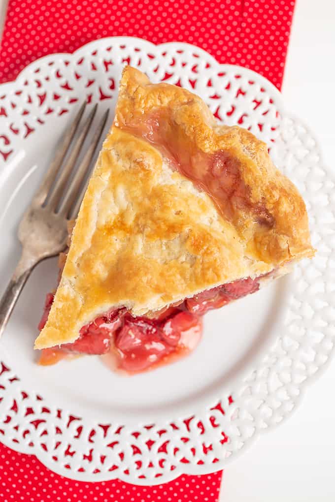 overhead photo of a slice of strawberry rhubarb pie on a plate with a fork with a red napkin under the plate