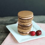 A stack of chocolate macarons on a white plate.