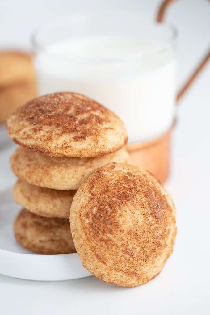 stacked cookies on a small white plate with a glass of milk and a cookie leaned against the stack of cookies