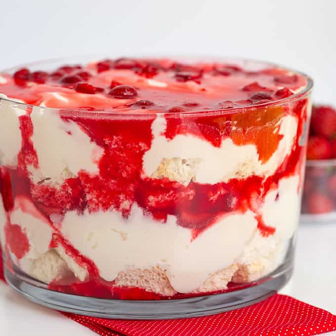 A glass bowl of Strawberry Angel Food Trifle with layers of sponge cake, custard, whipped cream, and strawberry sauce.