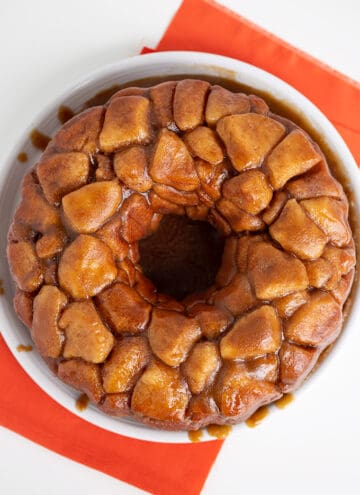 overhead photo of monkey bread on a white plate with an orange fabric under it