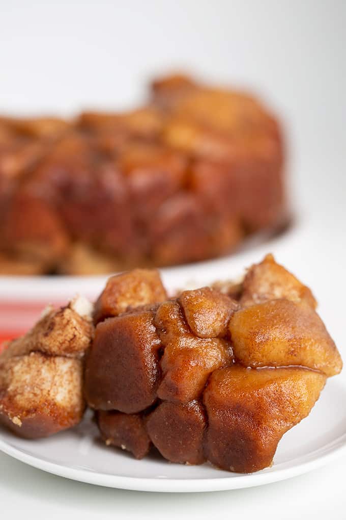 a small white plate with pieces of monkey bread on it and the whole serving plate of monkey bread behind it