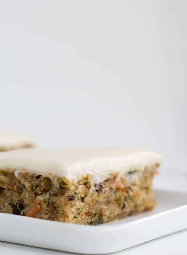 The Best Zucchini Bars - These are the best zucchini bars! They taste like a moist spice cake with a cream cheese frosting. You'll find cinnamon, shredded zucchini and carrots, and walnuts in these bars. This is one of the best zucchini recipes I can think of! #cookiedoughandovenmitt #zucchini #barrecipe #dessertfoodrecipes #dessertrecipes #creamcheesefrosting #frosting slice of zucchini and carrot spice cake with cream cheese frosting