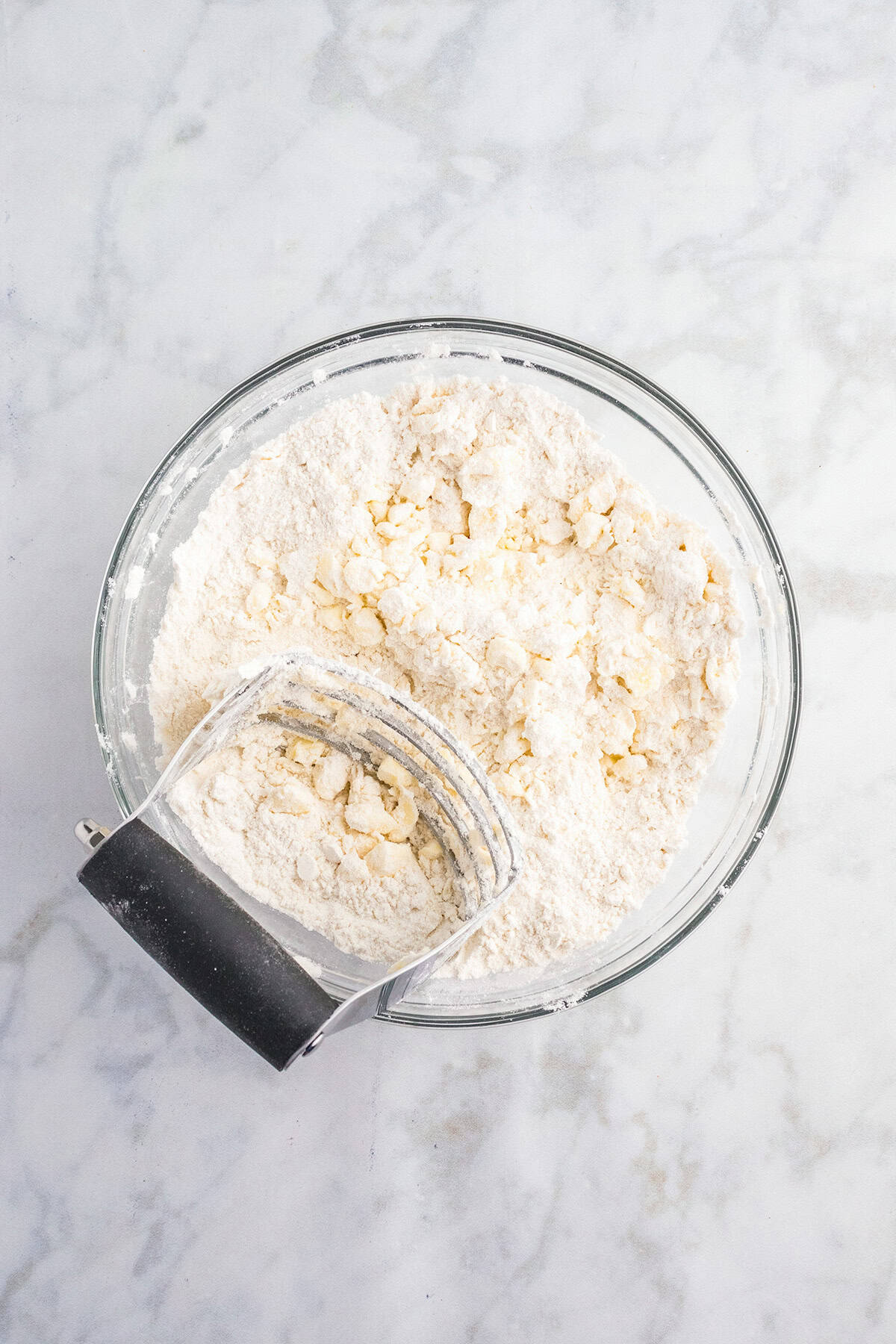 A glass bowl of flour and butter mixture with a pastry blender resting inside, on a marble surface—perfect for whipping up the buttery crust for Pecan Pie Bars.