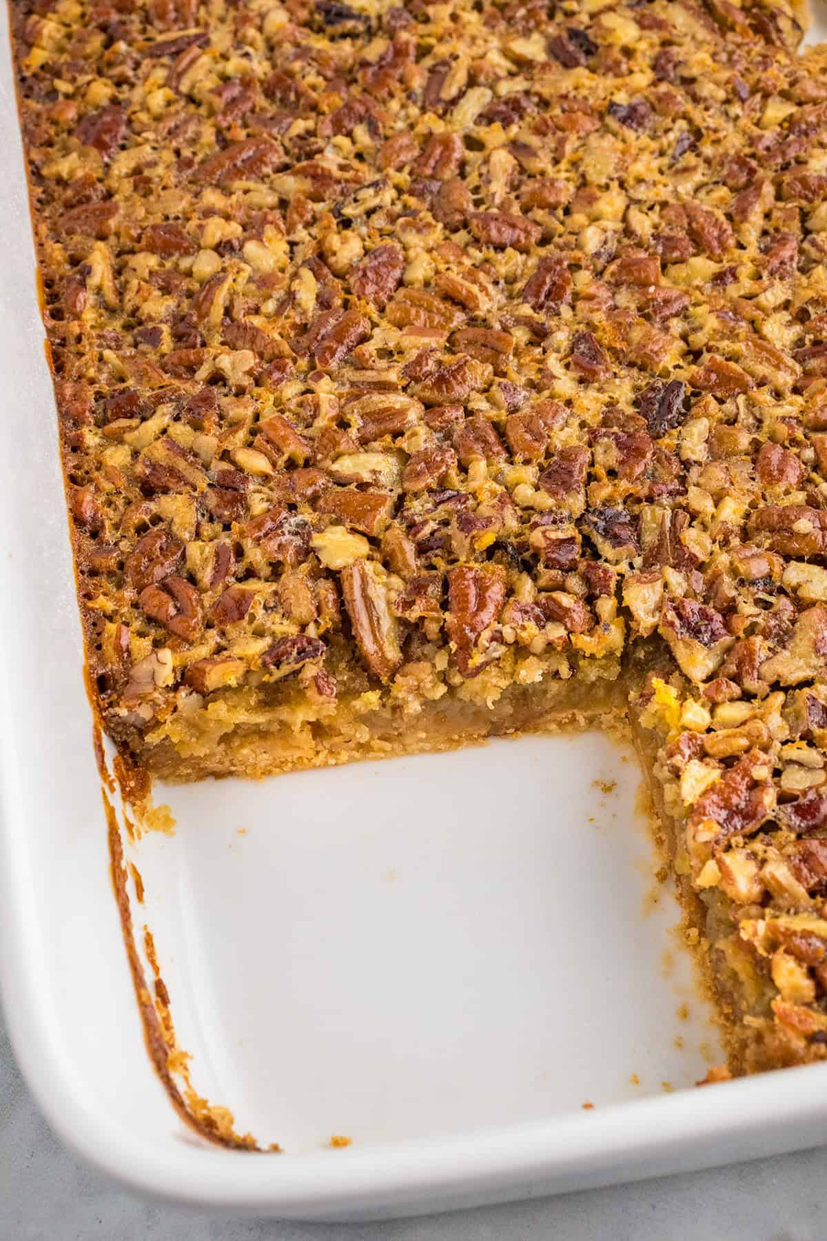 A rectangular dish of Pecan Pie Bars with a corner piece removed, revealing a gooey pecan filling and a golden crust.