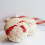 Two peppermint French macarons with red and white icing on a white paper.