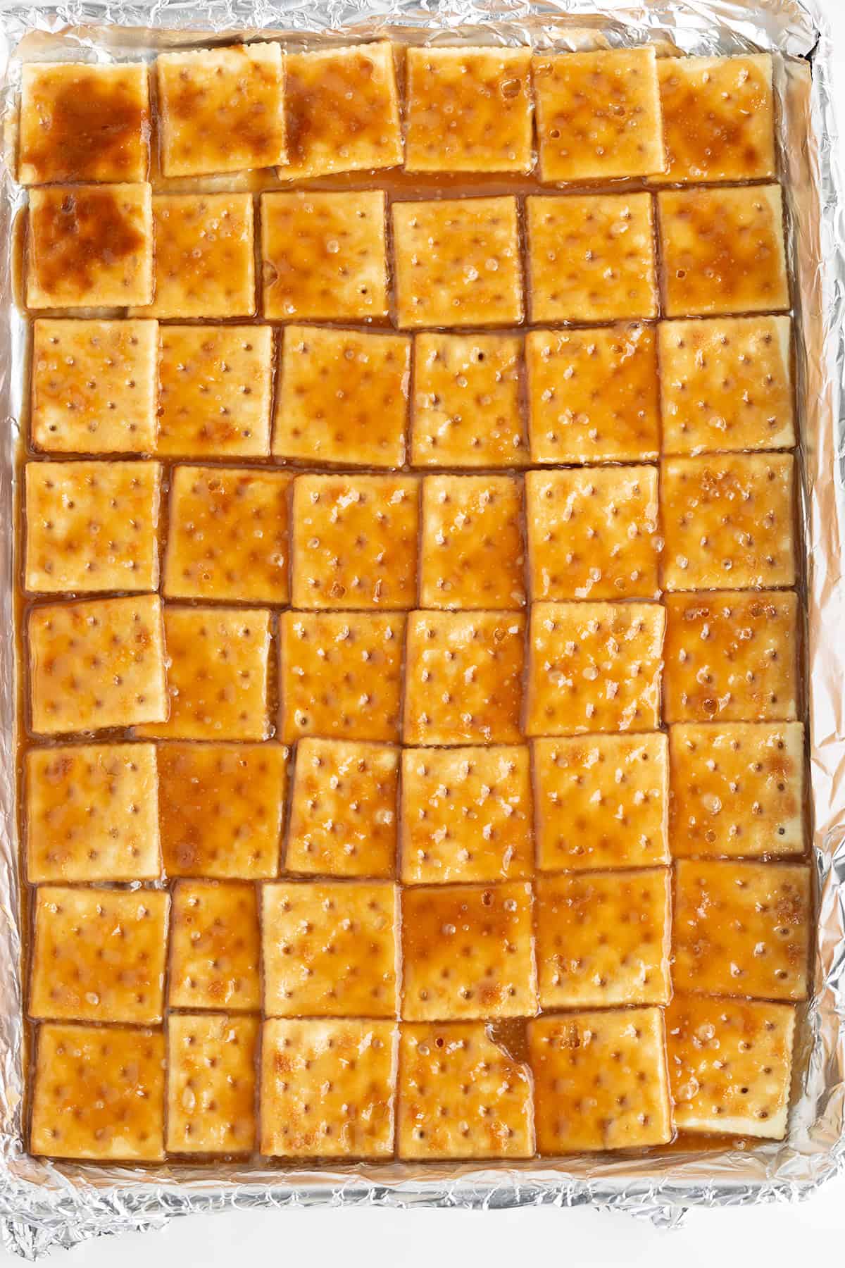 A tray of golden-brown Saltine Cracker Toffee glistens with caramel, perfectly arranged in a grid pattern on foil.