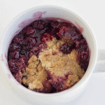 A blackberry crumble in a white cup.