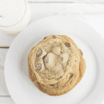 A stack of thin and chewy chocolate chip cookies on a white plate with a glass of milk.
