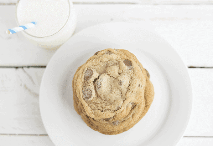 A stack of thin and chewy chocolate chip cookies on a white plate with a glass of milk.