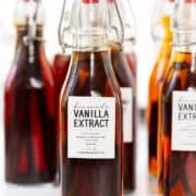 Several glass bottles filled with homemade vanilla extract, each labeled and sealed with a swing-top cap, are arranged on a white surface—perfect for showcasing the rich color of your homemade vanilla extract.