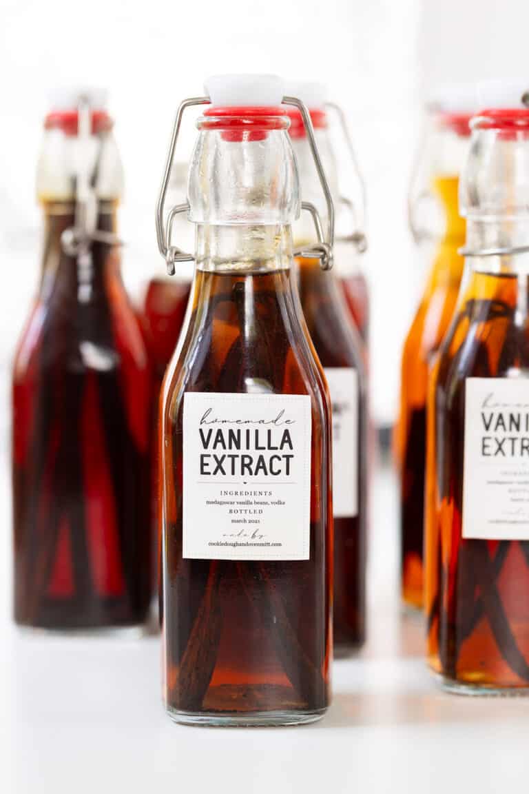 Several glass bottles filled with homemade vanilla extract, each labeled and sealed with a swing-top cap, are arranged on a white surface—perfect for showcasing the rich color of your homemade vanilla extract.