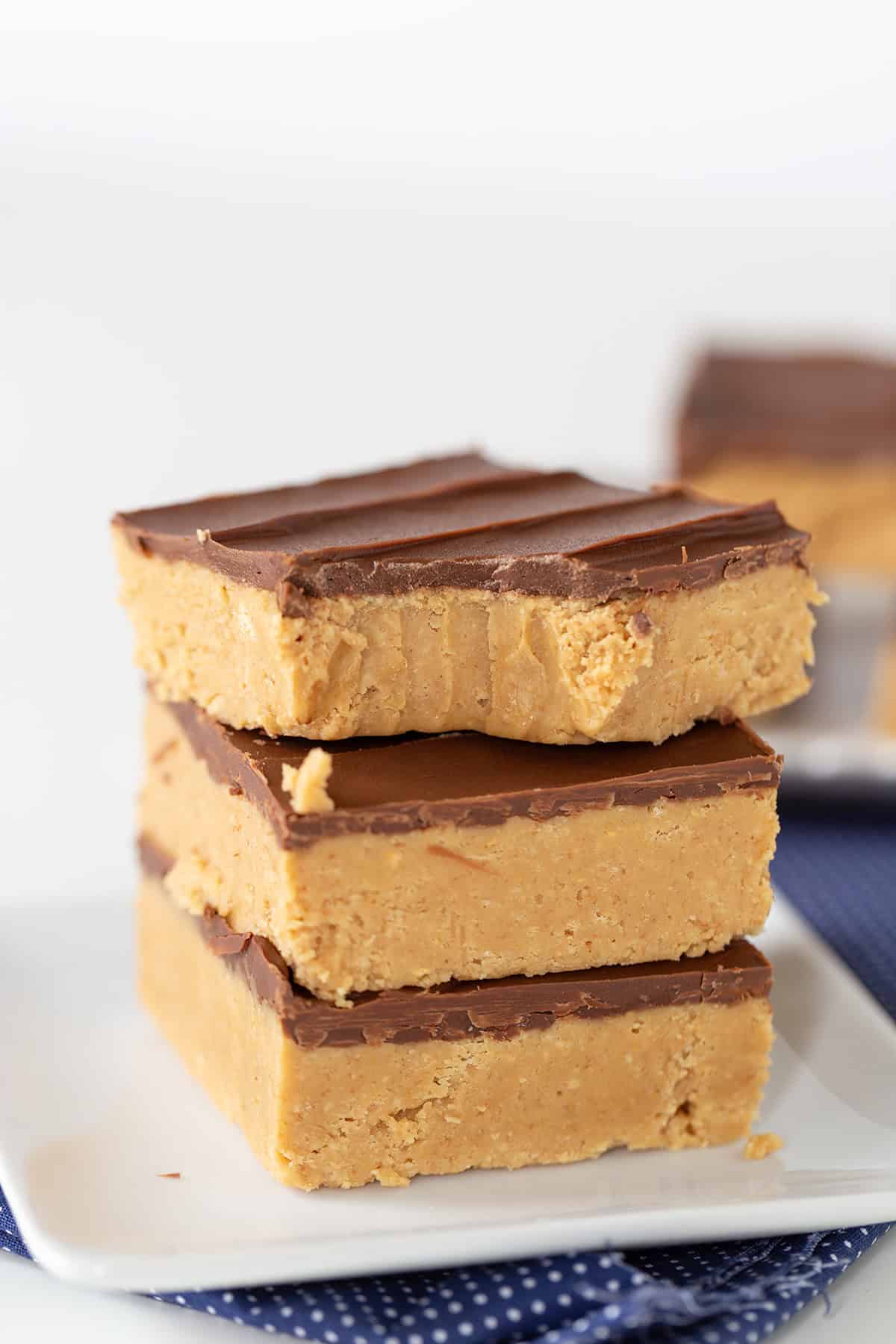 A stack of three luscious peanut butter bars with a chocolate topping is placed on a white plate.