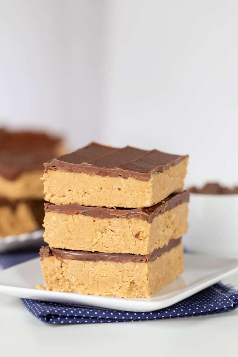 Three stacked Peanut Butter Bars on a white plate with more bars visible in the background.