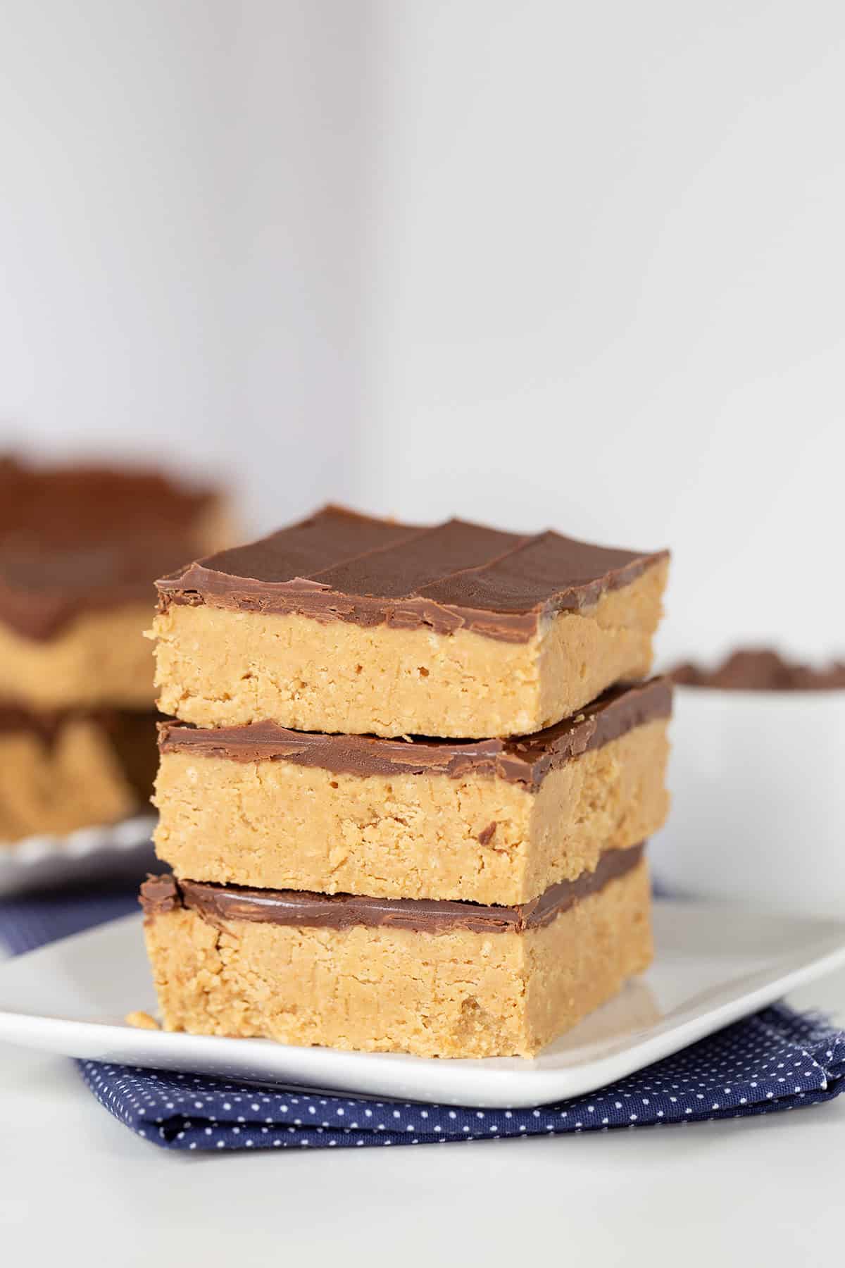 Three stacked Peanut Butter Bars on a white plate with more bars visible in the background.