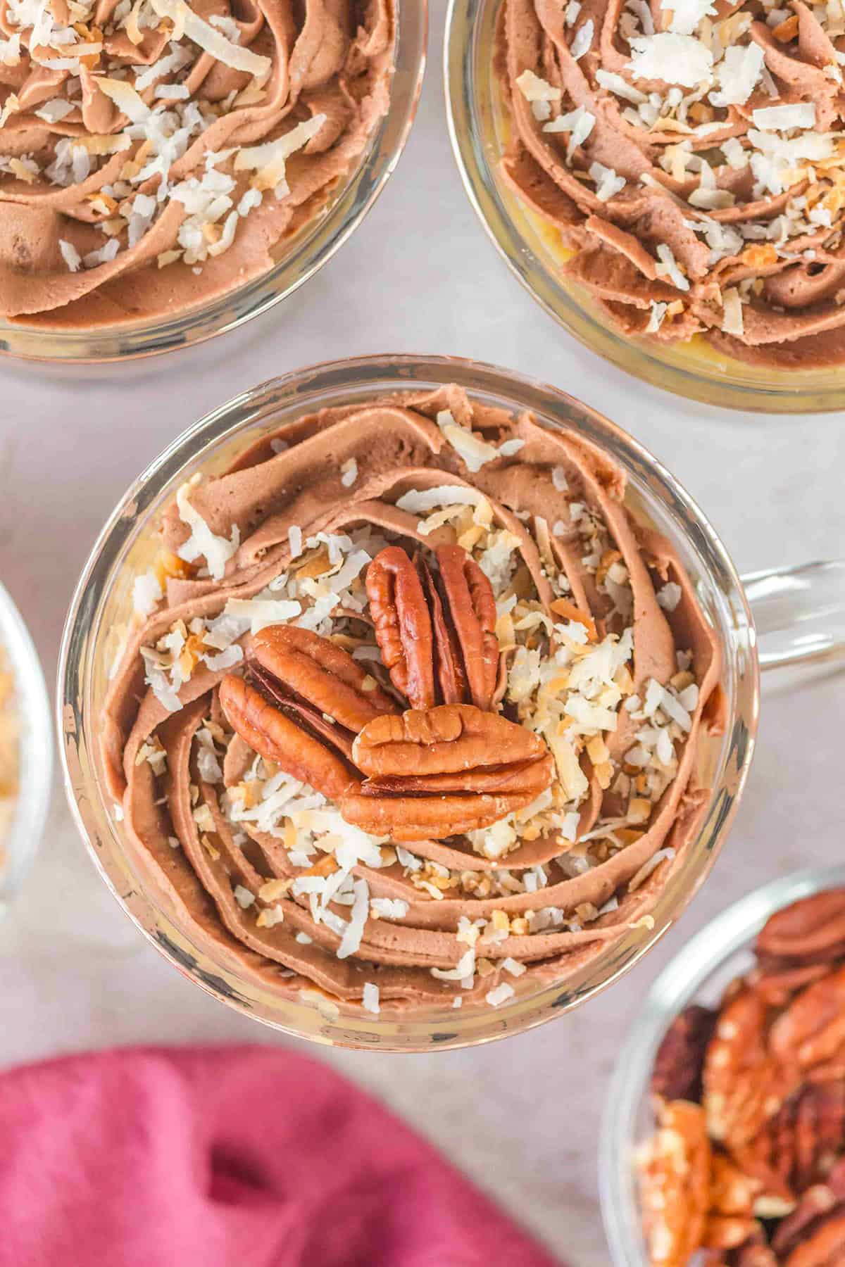 Indulge in a German Chocolate Trifle with rich chocolate mousse, topped with crunchy pecans and delicate shredded coconut, served elegantly in glass cups.