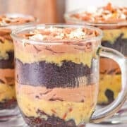 Glass mug filled with layers of German Chocolate Trifle, featuring rich chocolate cake, creamy yellow pudding, and velvety chocolate mousse, all topped with crunchy nuts.
