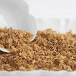 A brown granules-filled white bowl showcasing toasted coconut.