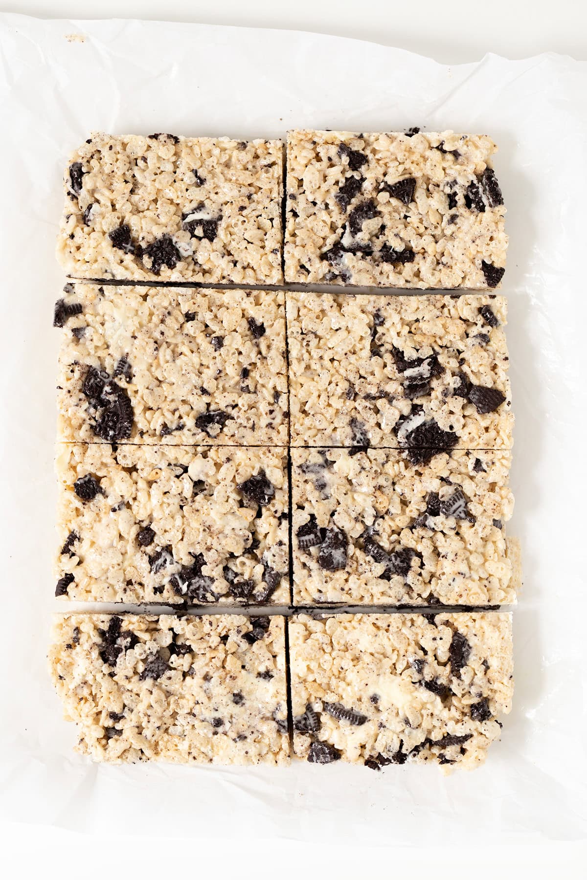 Cookies & Cream Rice Crispy Treats are cut into eight rectangular pieces and arranged on white parchment paper.