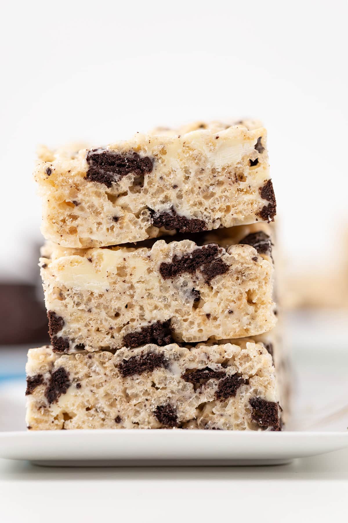 Three stacked Cookies & Cream Rice Crispy Treats with visible chocolate cookie pieces rest on a white plate.