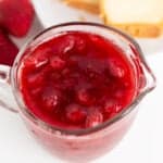 overhead image of a serving glass with strawberry syrup in it with pound cake behind it on a white surface