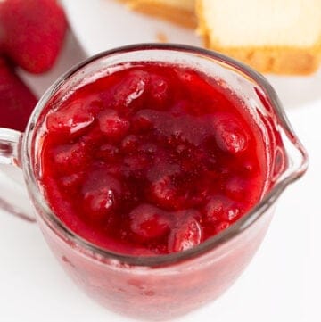 overhead image of a serving glass with strawberry syrup in it with pound cake behind it on a white surface