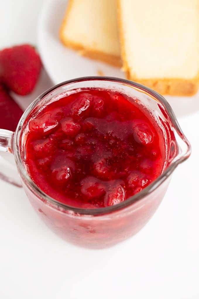 overhead image of a serving glass with strawberry syrup in it with pound cake behind it on a white surface