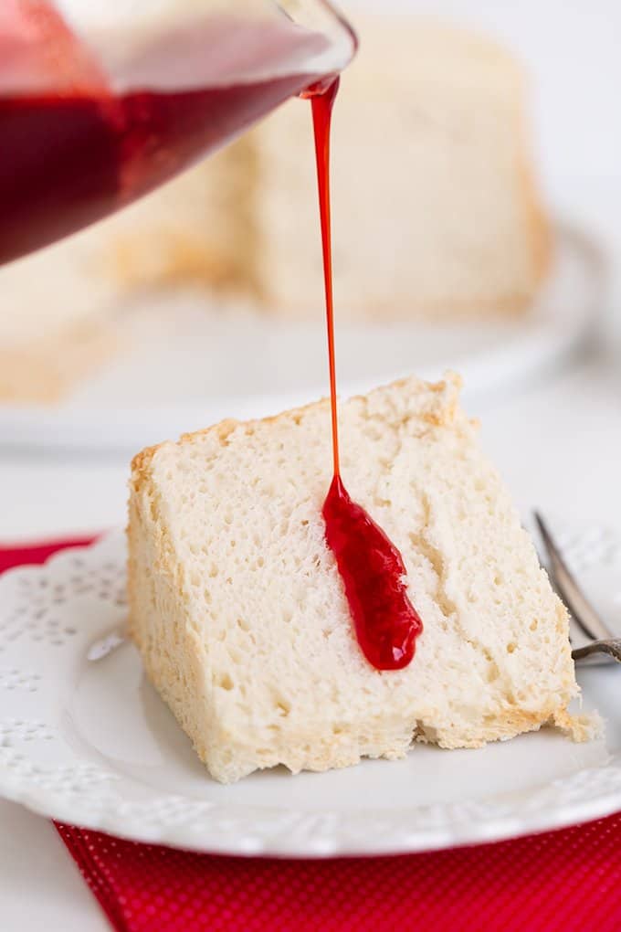 pouring syrup on a slice of angel food cake on a white plate with a red linen