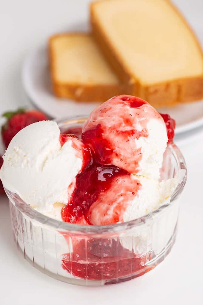 vanilla ice cream in a glass bowl with strawberry syrup on it and pound cane behind it