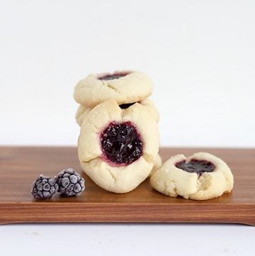 A stack of Blackberry Thumbprints cookies on a wooden cutting board.