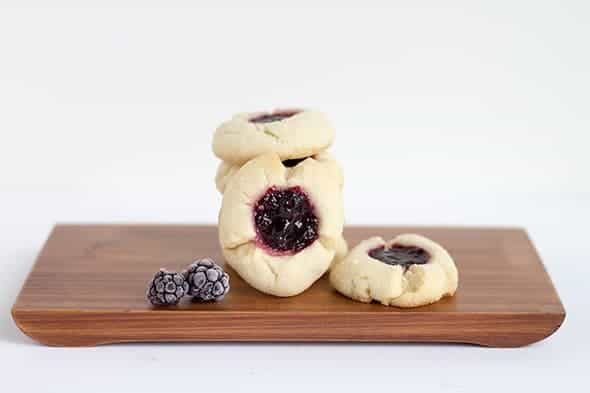 A stack of Blackberry Thumbprints cookies on a wooden cutting board.