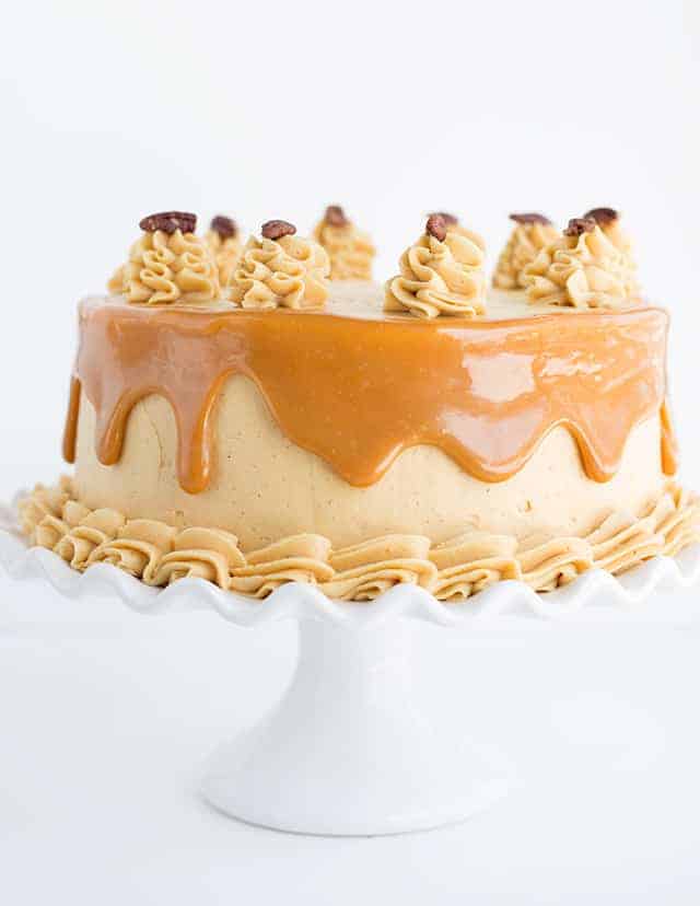 Side shot of carrot cake with caramel buttercream on a white ruffled cake plate. 