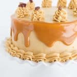 Carrot cake with caramel buttercream on a white ruffled cake plate.