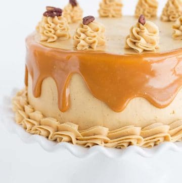 Photo of carrot cake with caramel buttercream on a white ruffled cake plate.