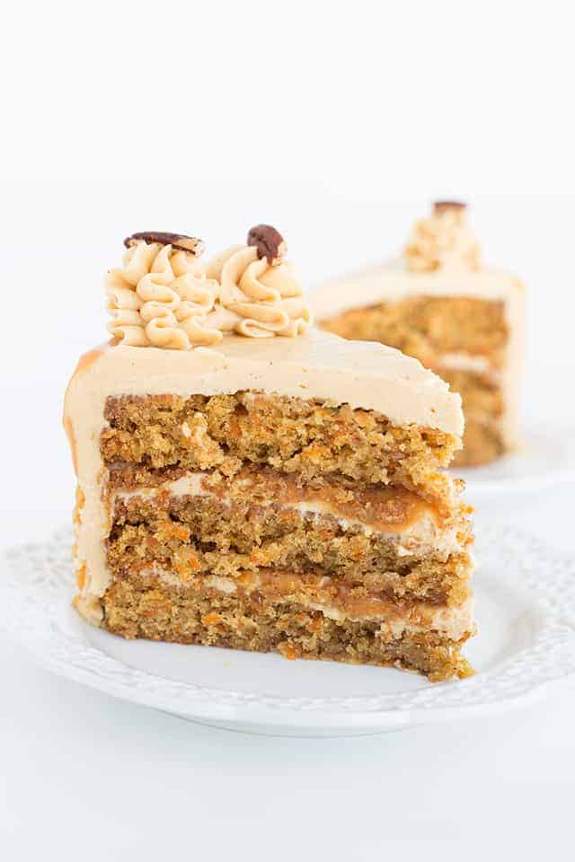 Slice of carrot cake with caramel buttercream on a white dessert plate showing the buttercream and caramel layers.